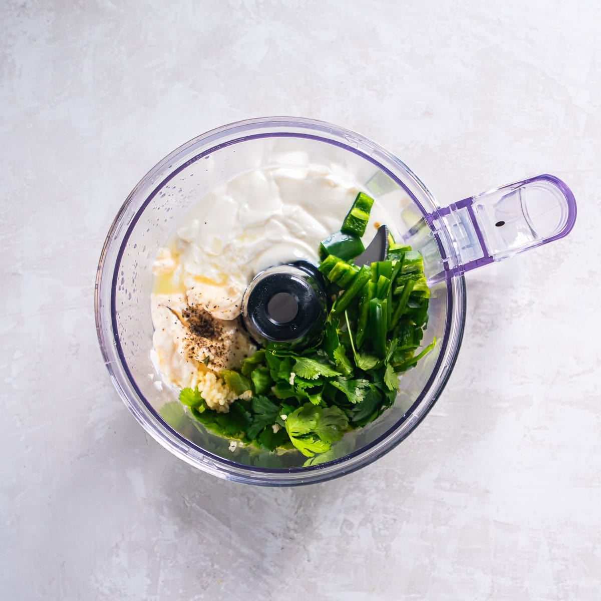 Cilantro lime sauce ingredients in a food processor including sour cream, mayonnaise, cilantro, jalapeño, garlic, and lime juice before blending.