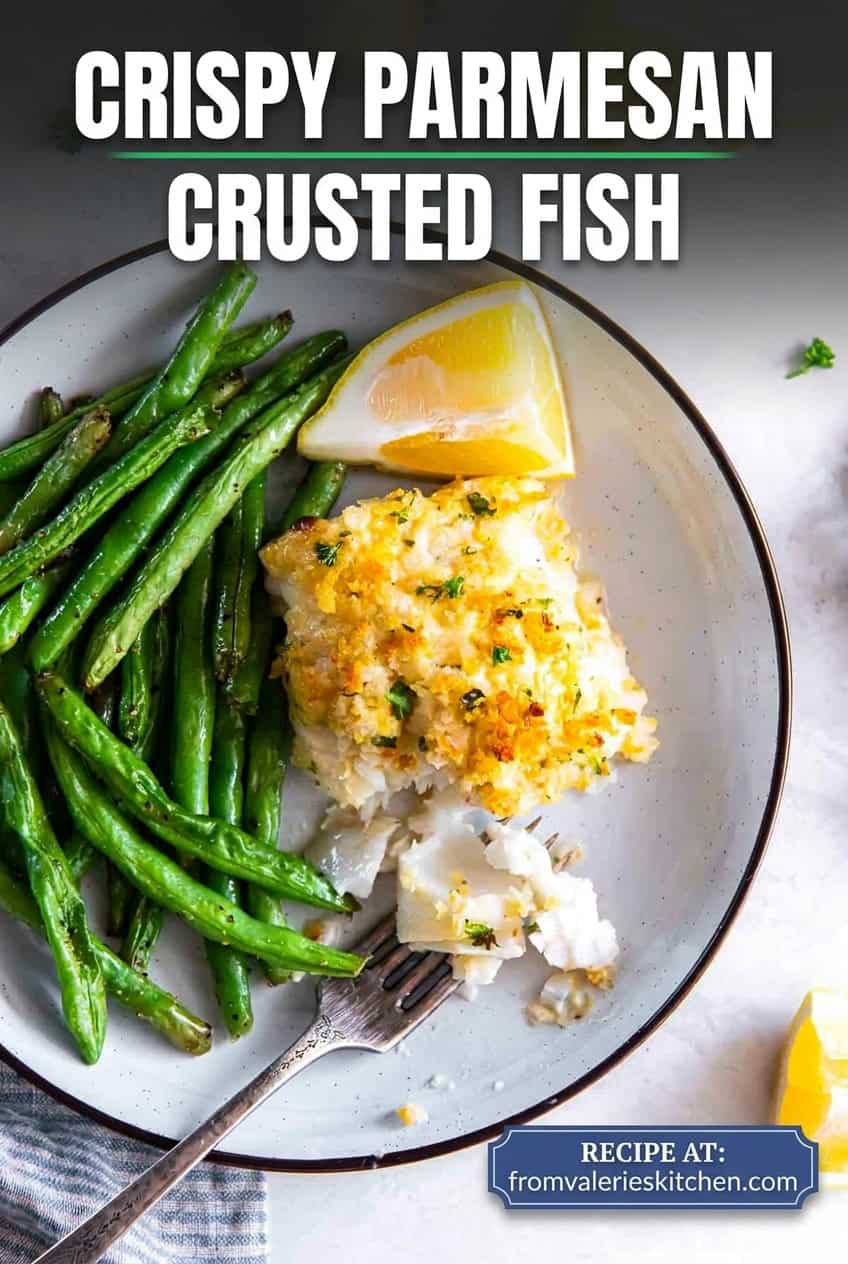 Flaky Parmesan crusted fish served with green beans and lemon wedges, with a fork breaking into the fish with text overlay.