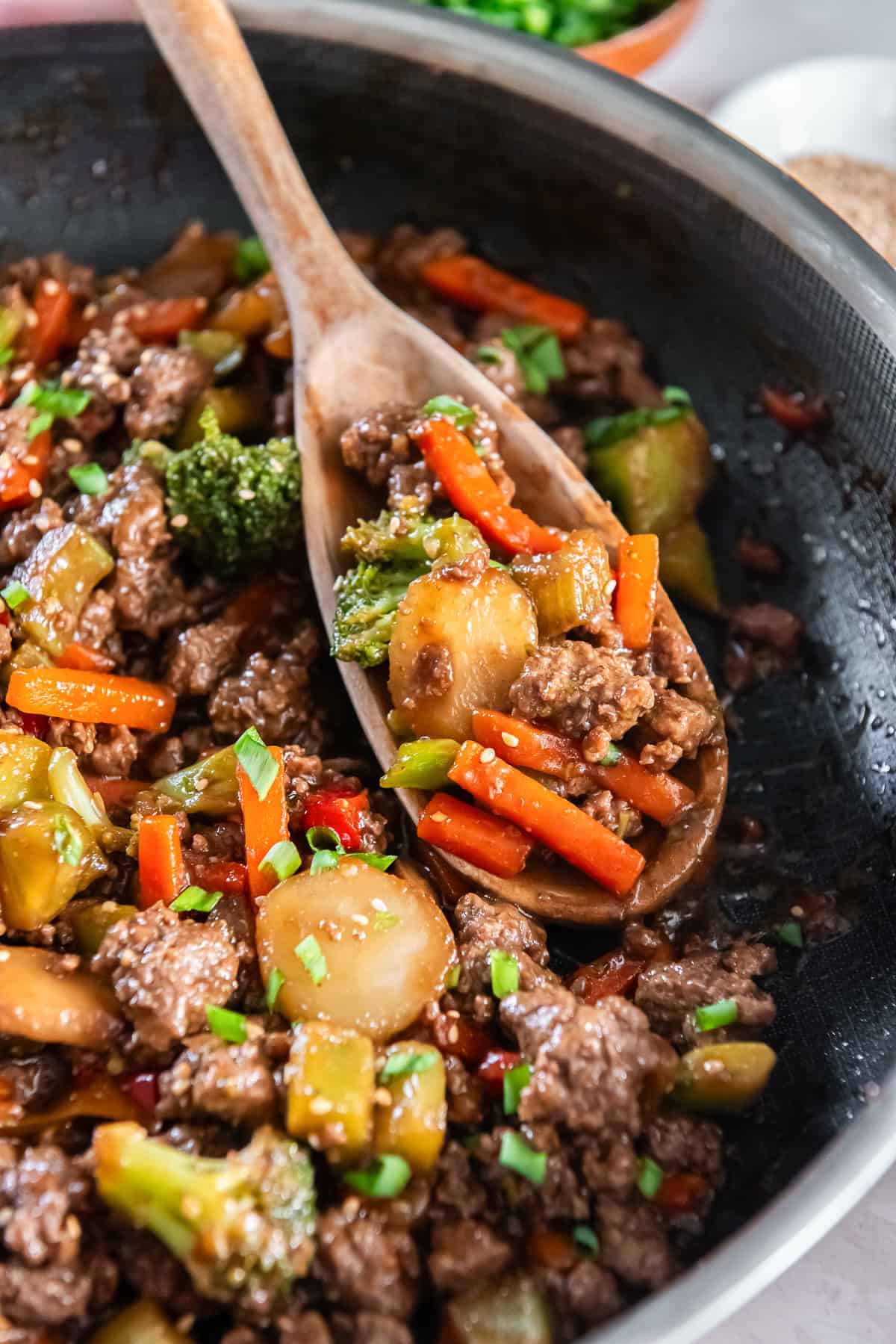 Spoonful of ground beef teriyaki with vegetables in skillet.