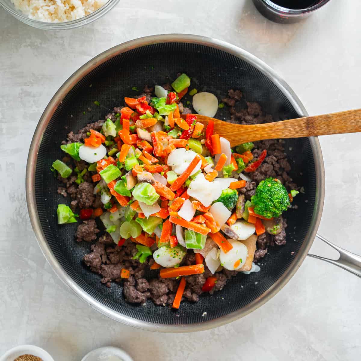 Adding frozen stir-fry vegetables to cooked ground beef in skillet.