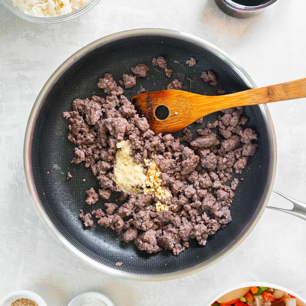 Cooked ground beef in skillet with garlic and ginger added.
