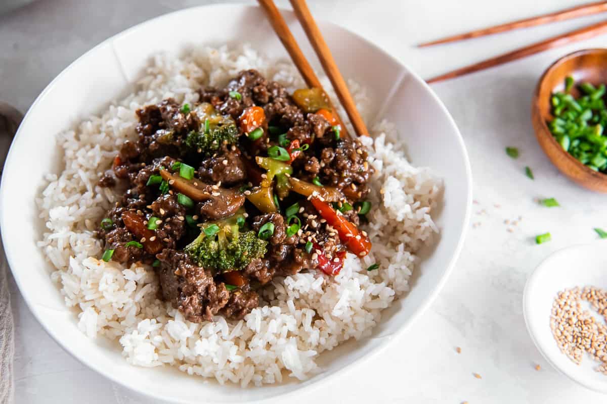 Ground beef teriyaki bowls with rice, vegetables, sesame seeds, and chopsticks