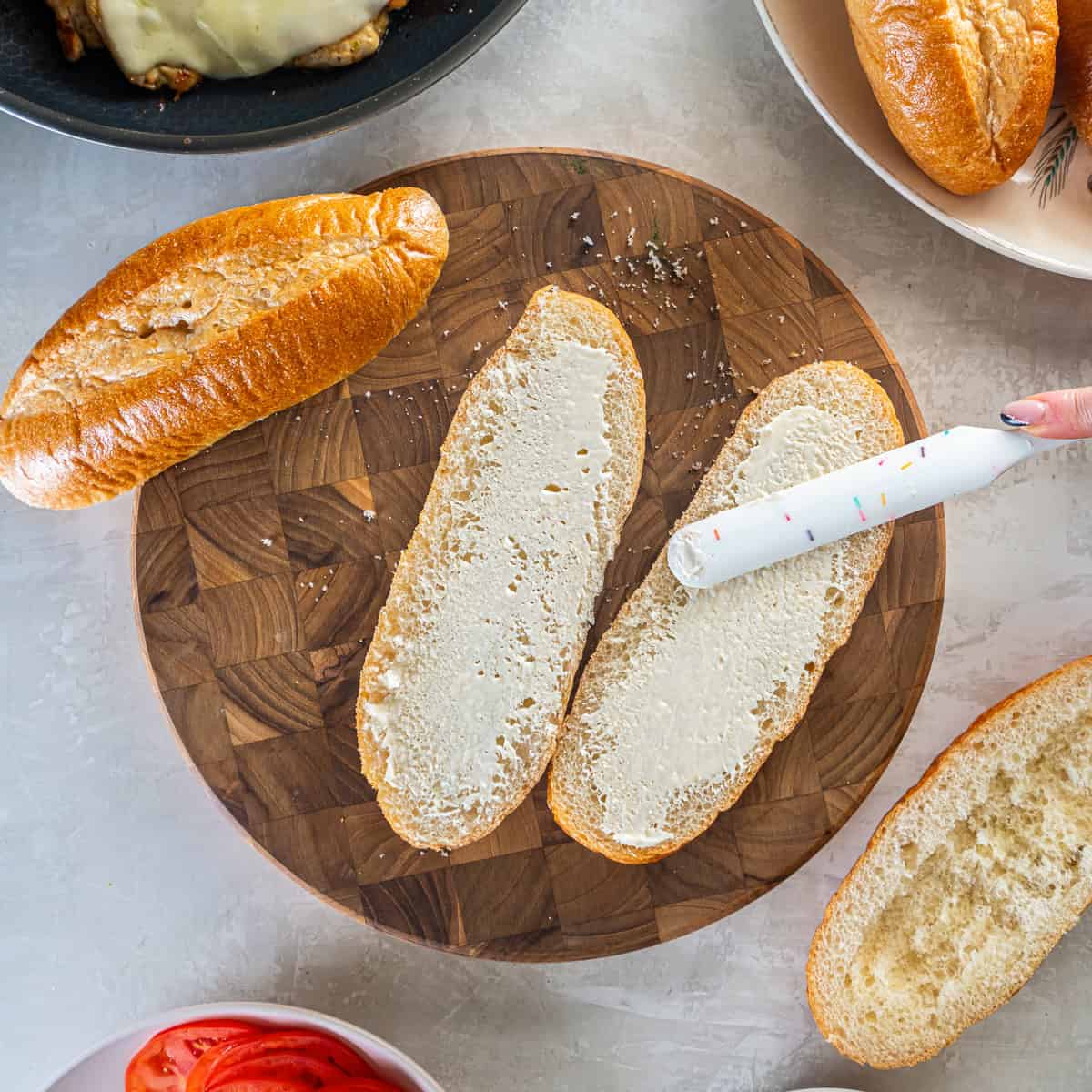 Spreading mayonnaise on sliced sub rolls.