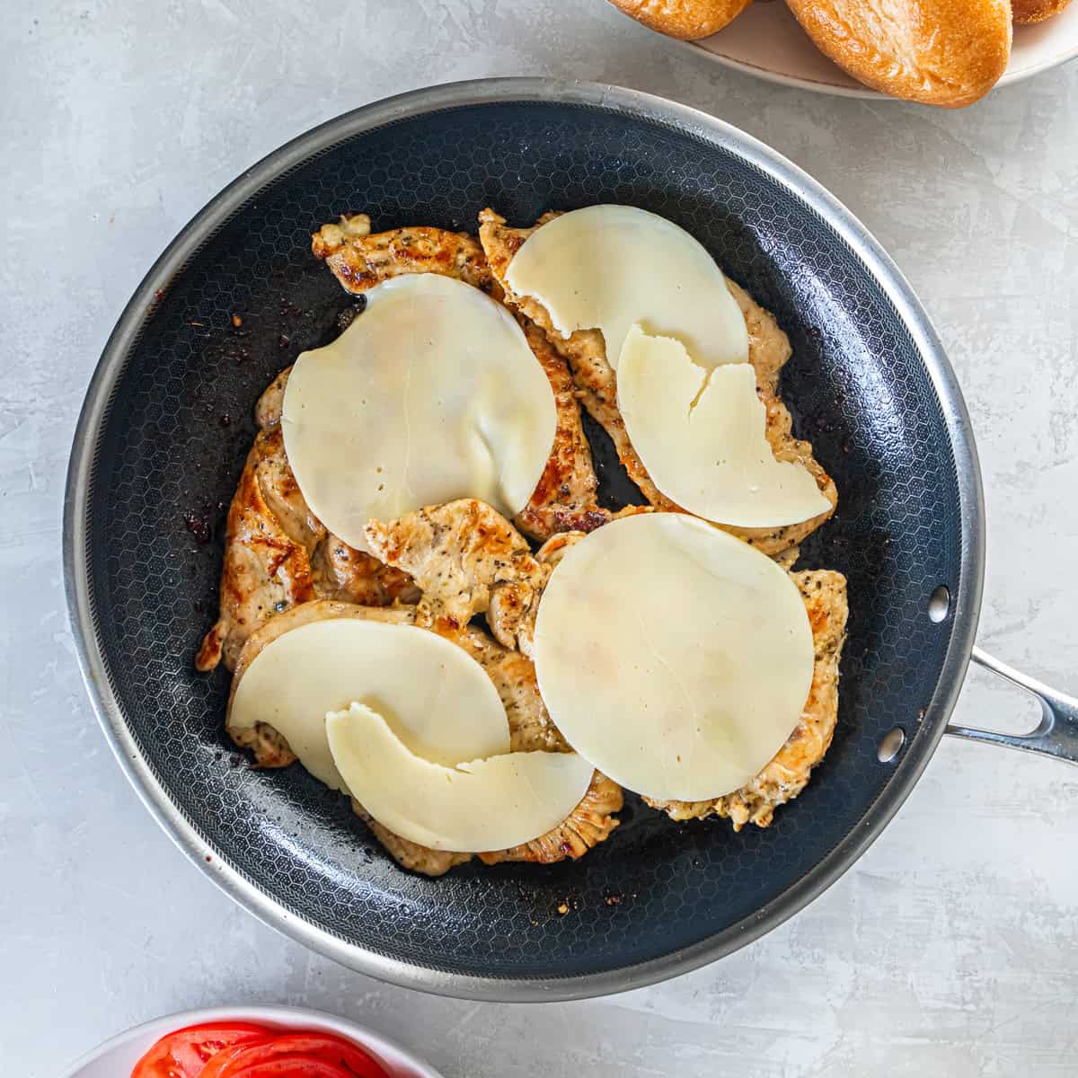 Provolone cheese melting over cooked chicken in a skillet.