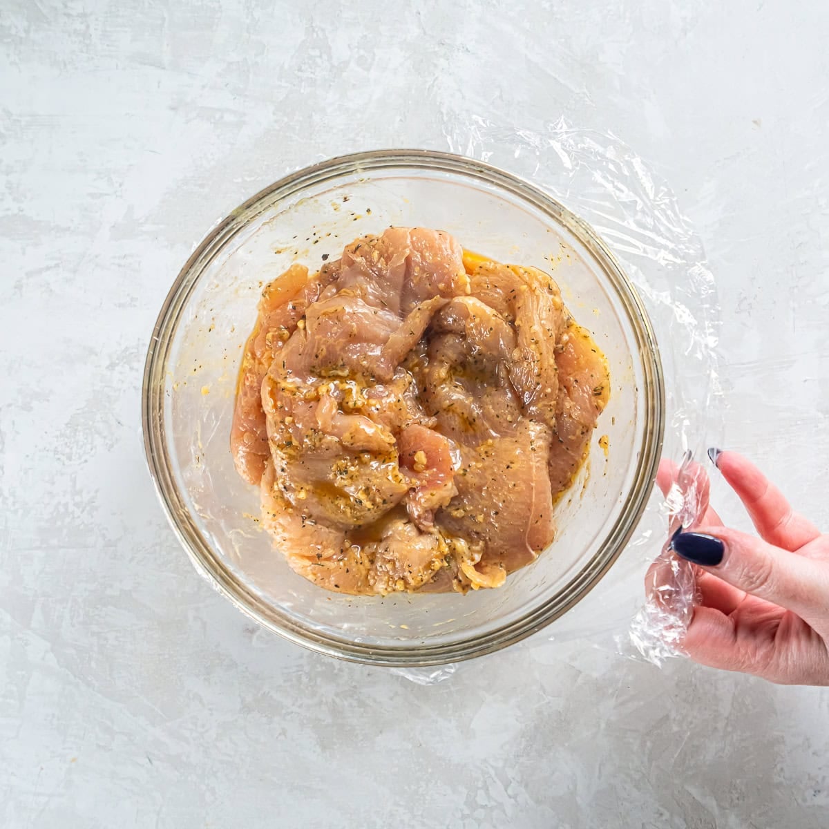 Chicken marinating in a bowl with Italian seasoning, olive oil, mustard, and garlic for Italian chicken sub sandwiches.