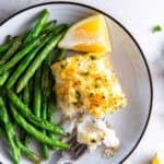 Flaky Parmesan crusted fish served with green beans and lemon wedges, with a fork breaking into the fish.