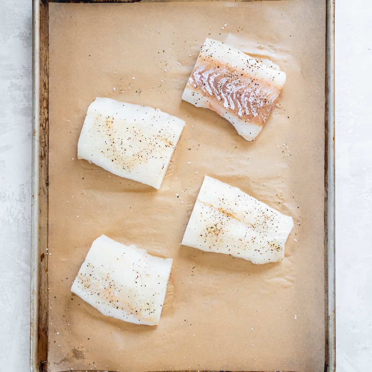 White fish fillets arranged on a parchment-lined baking sheet and seasoned with salt and pepper.