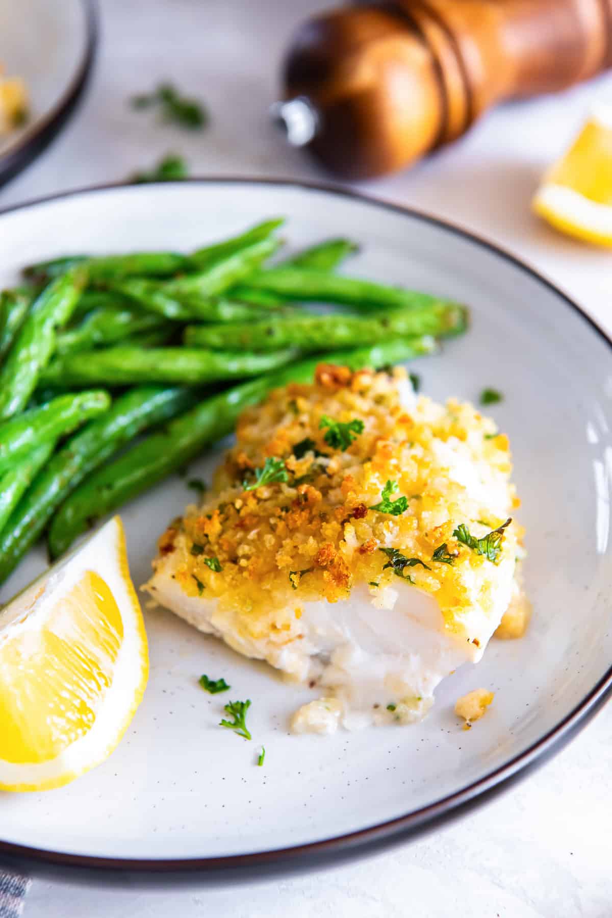Parmesan crusted fish served with green beans and lemon wedges on a plate.