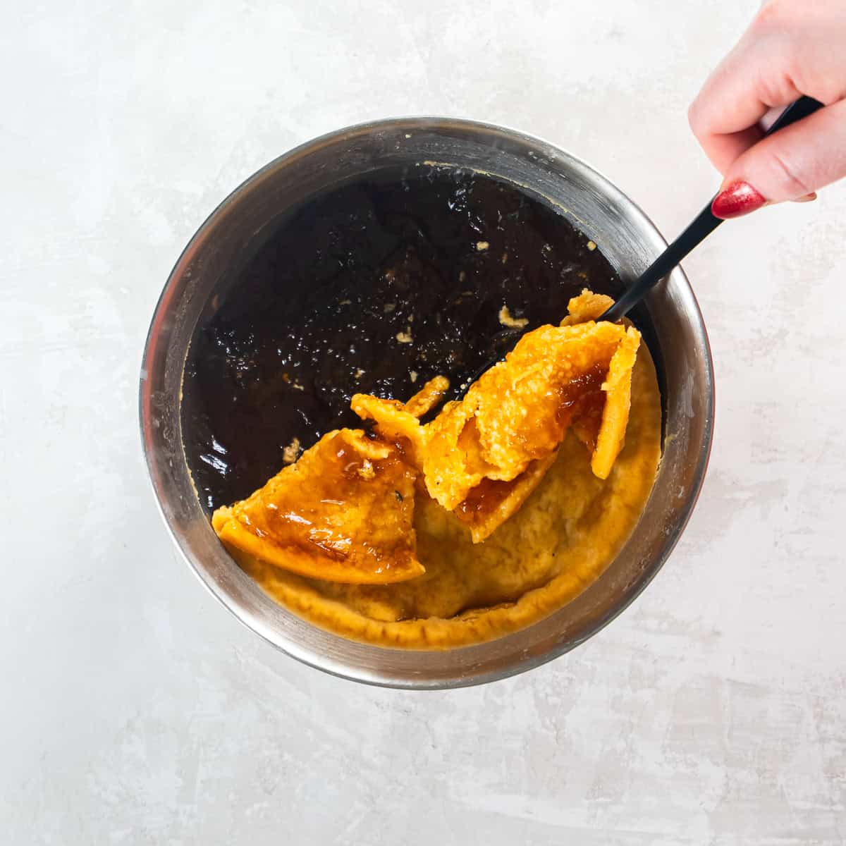 Solidified fat being lifted from chilled cooking liquid with a spoon.