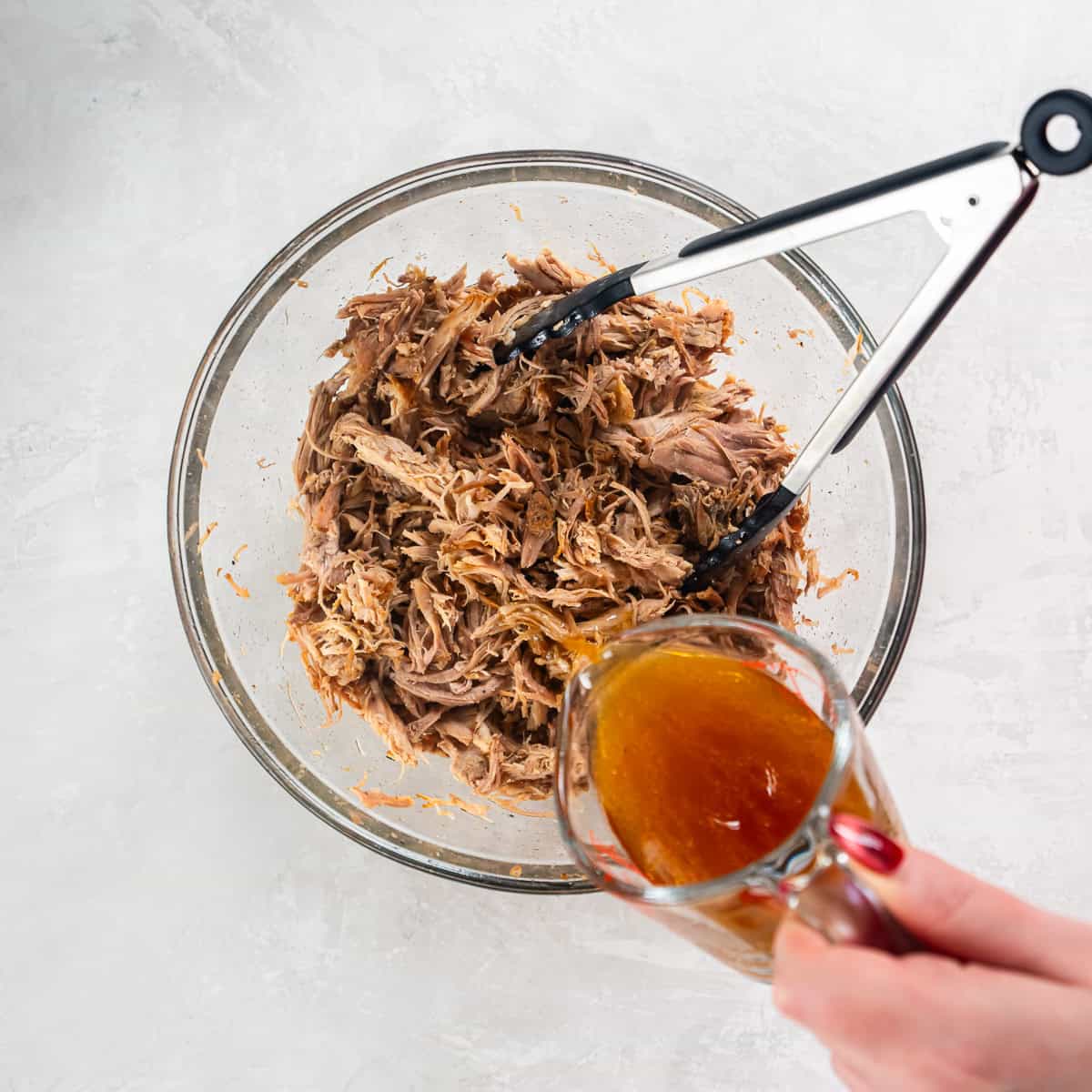 Shredded pulled pork being moistened with juices in a bowl.