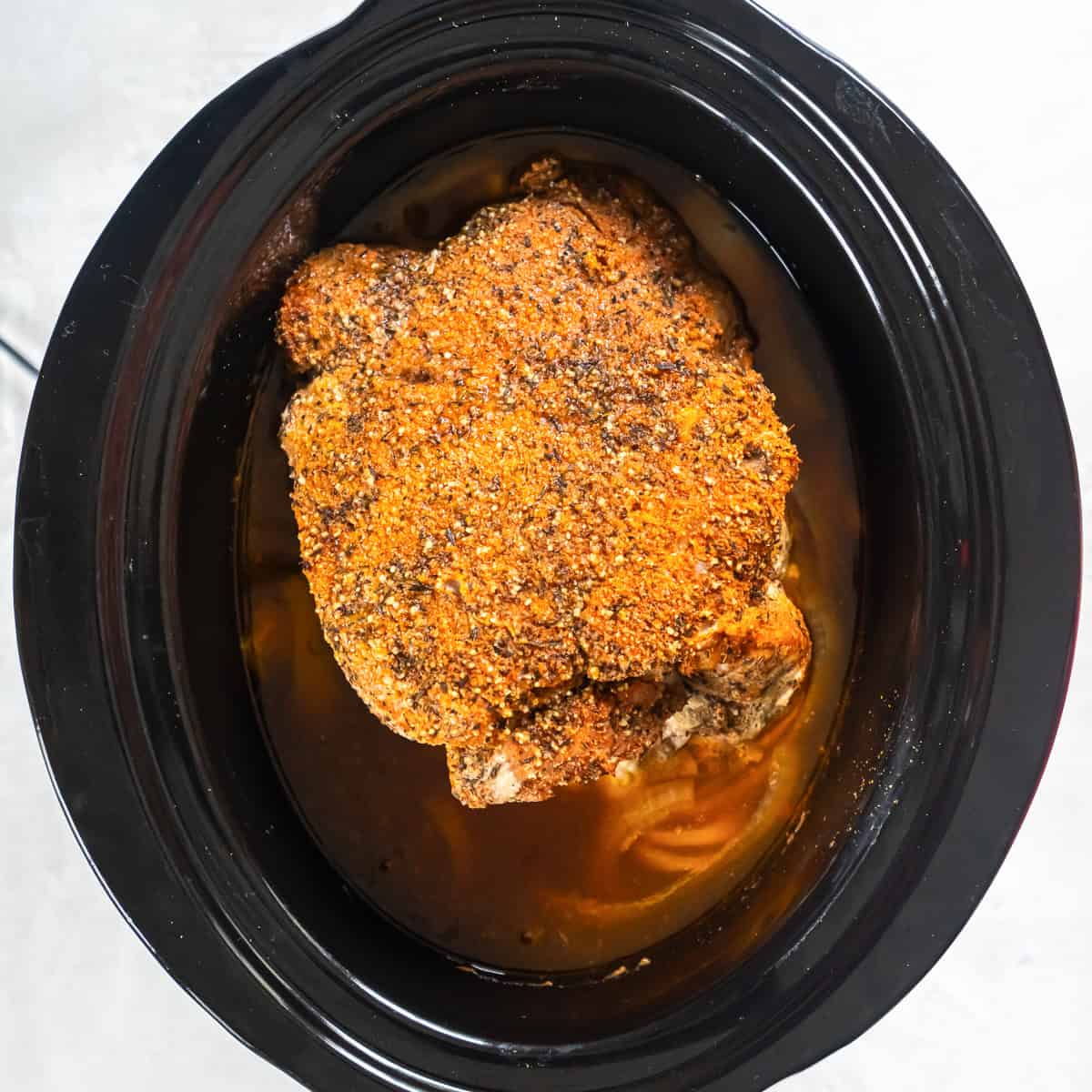 Cooked pork shoulder in a slow cooker after cooking, ready to shred.