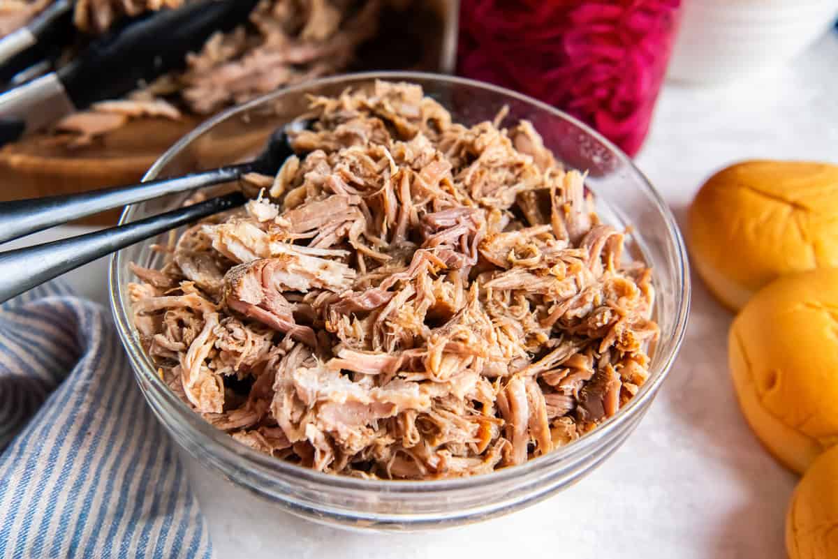 Tongs resting in a bowl of pulled pork.