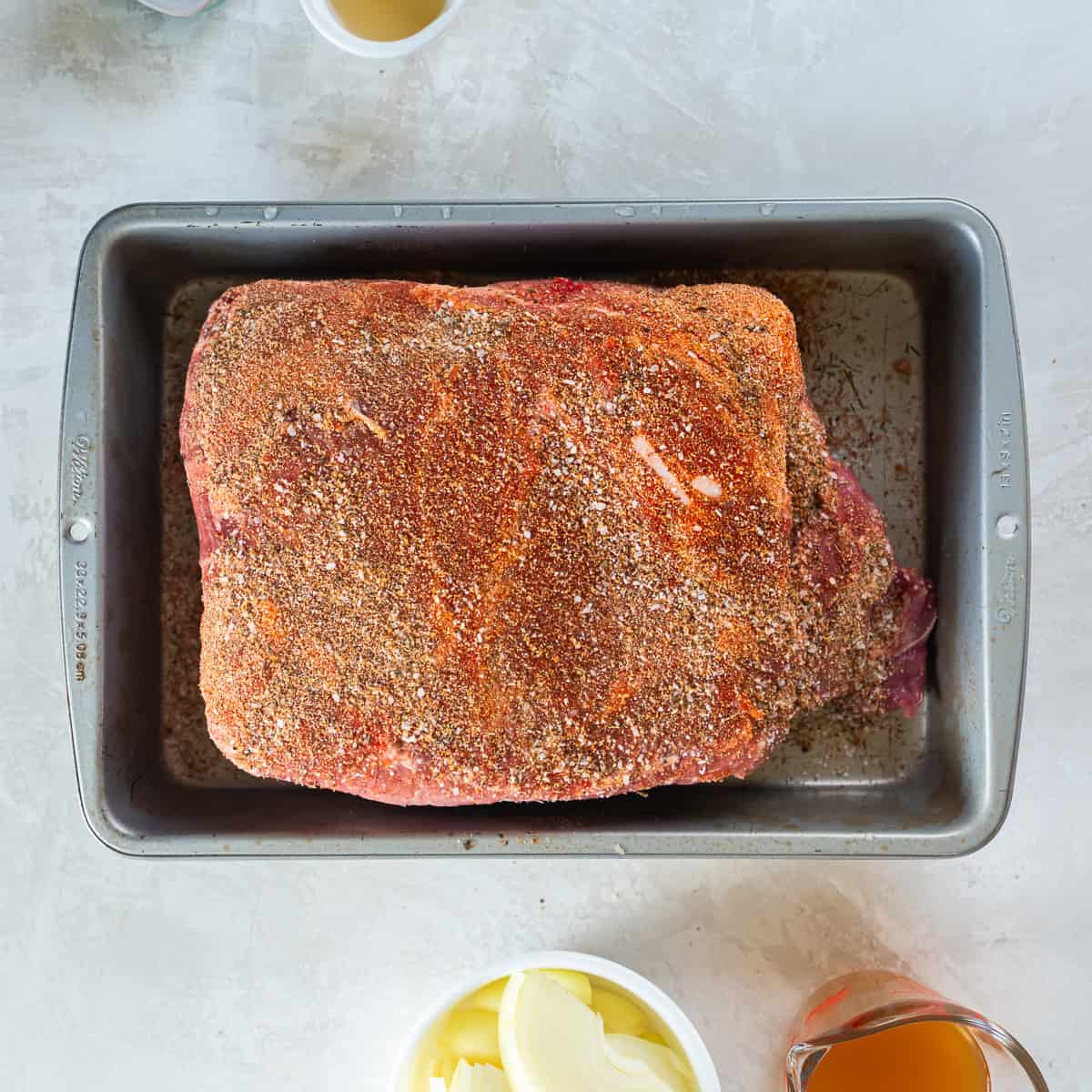 Pork shoulder coated with spice rub in a baking dish before cooking.