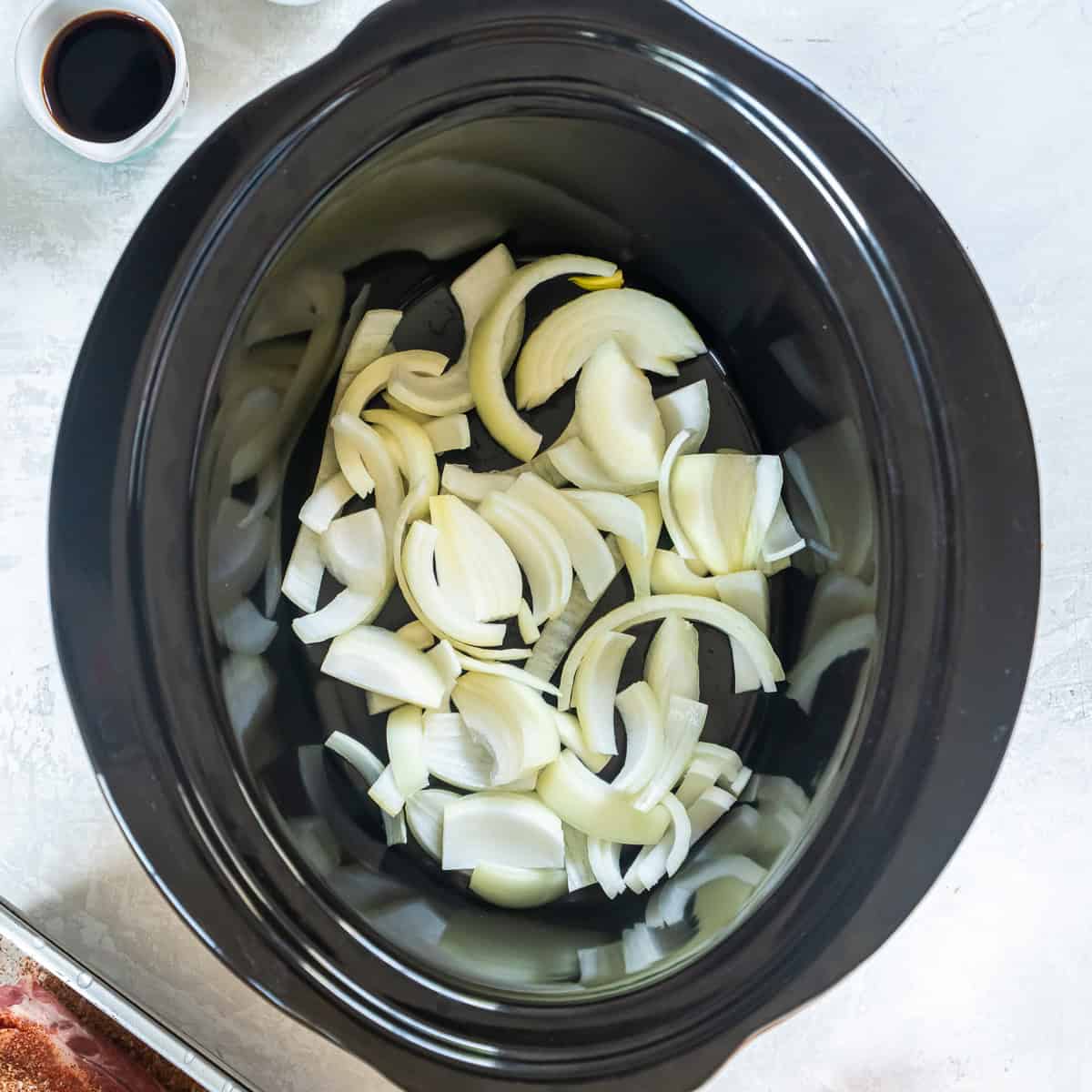 Sliced onions placed in the bottom of a slow cooker.