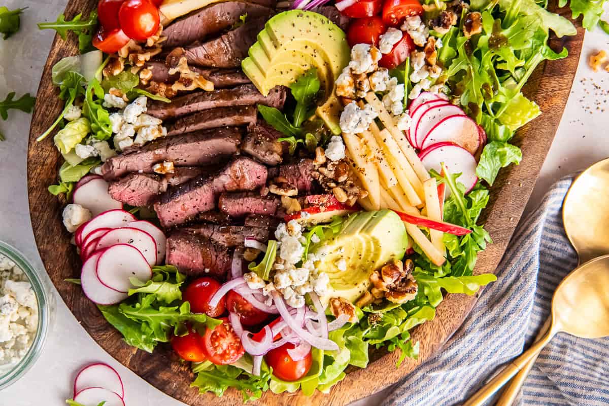 Steak salad with sliced sirloin, apple, avocado, blue cheese, tomatoes and walnuts on top of fresh vegetables.