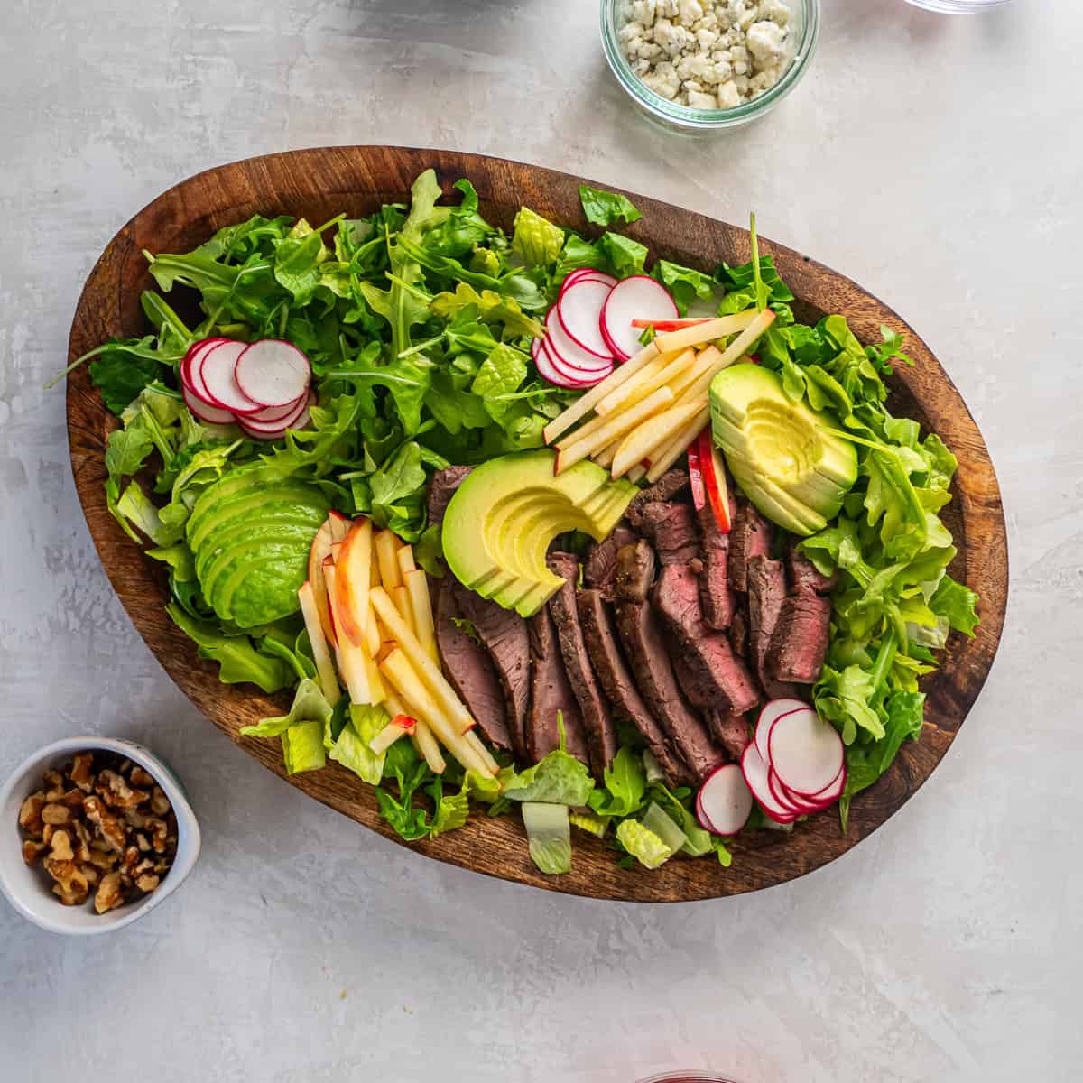 Steak salad topped with sliced avocado, apple matchsticks, and radishes.