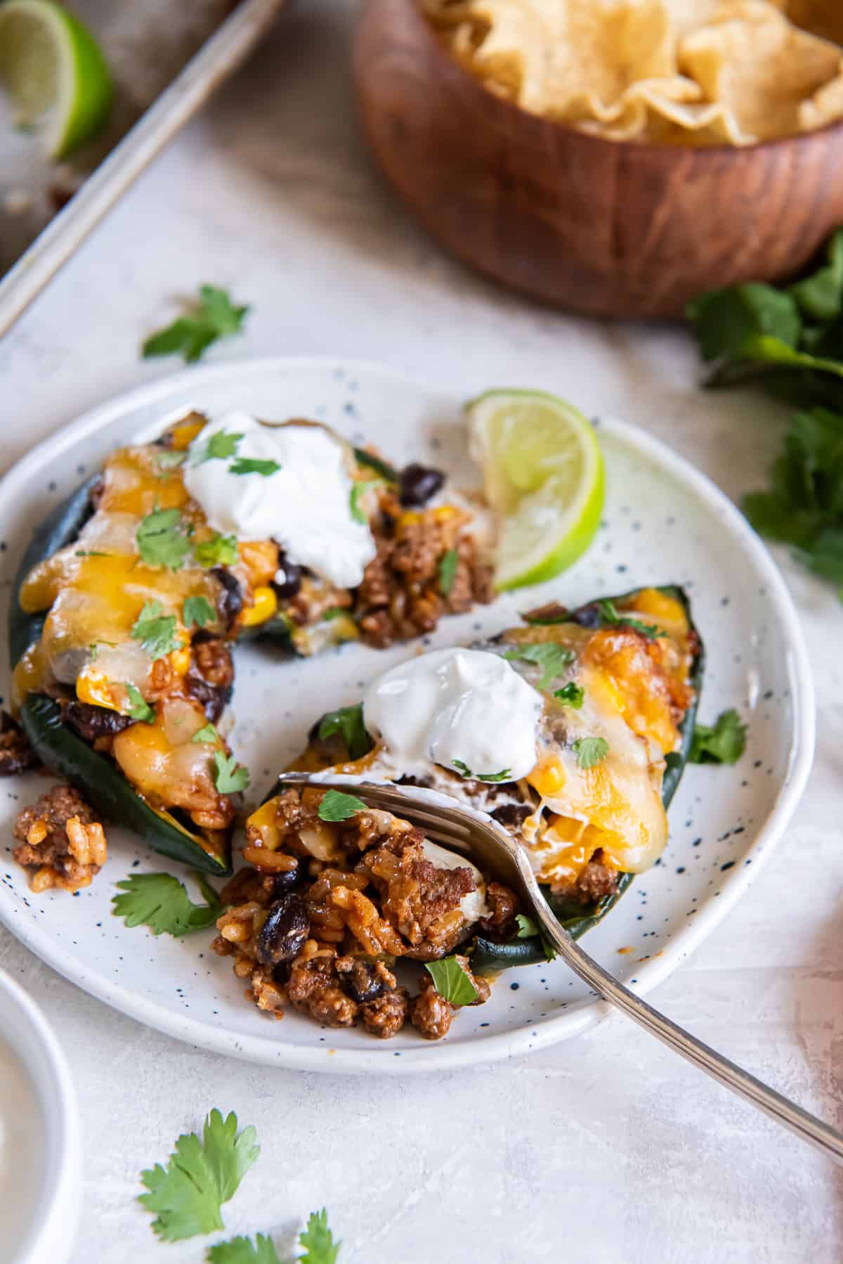 baked stuffed poblano pepper halves filled with ground beef, rice, black beans, and corn, topped with melted cheese and garnished with cilantro, with lime wedges on a sheet pan.