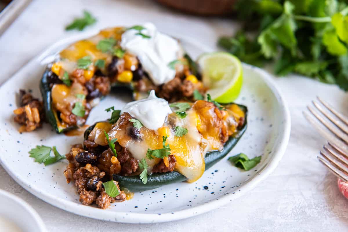 Stuffed poblano pepper on a plate topped with melted cheese, sour cream, and cilantro, with a lime wedge on the side.