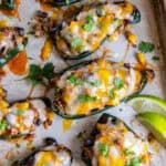 Sheet pan of baked stuffed poblano peppers filled with ground beef, rice, black beans, and corn, topped with melted cheese and garnished with cilantro and lime wedges.