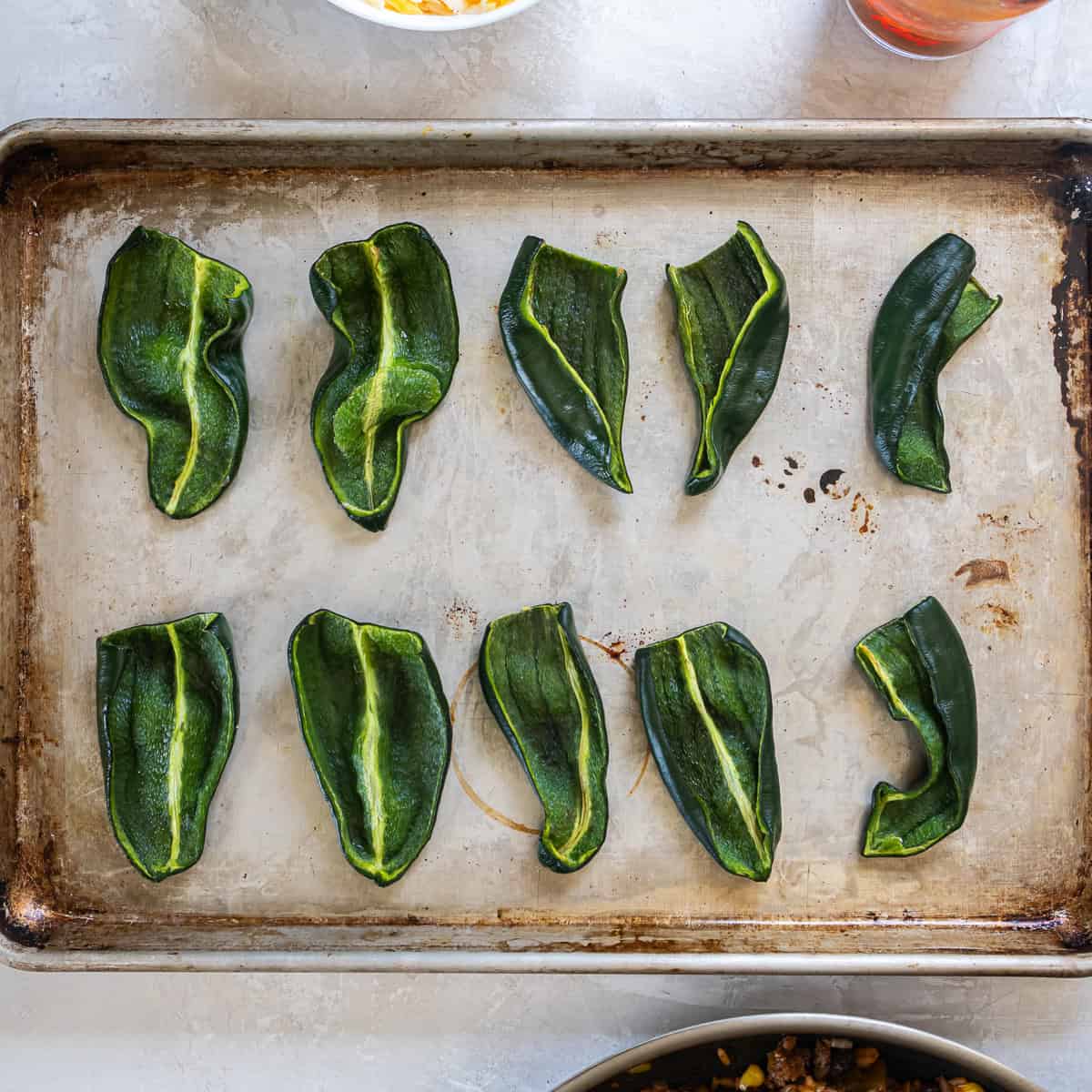 Halved poblano peppers roasted on a baking sheet,
