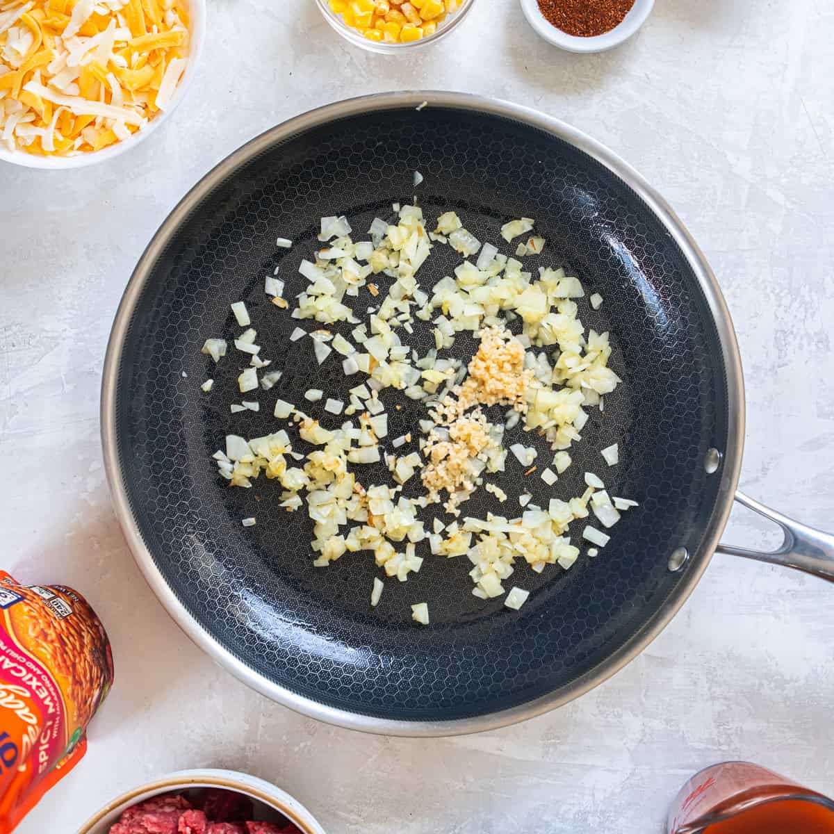 Diced onion and minced garlic cooking in a skillet with olive oil.