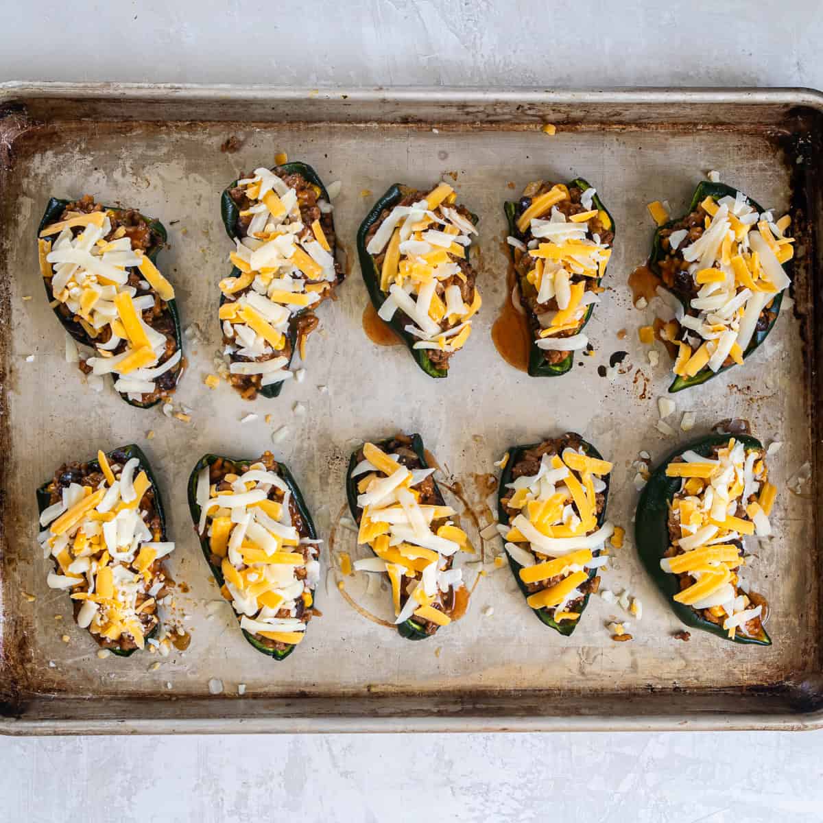 Stuffed poblano peppers topped with shredded cheese on a baking sheet.