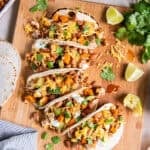 Chicken tacos with roasted sweet potatoes, cauliflower, and zucchini topped with pinto beans, shredded cheese, sour cream, and fresh cilantro on a wooden board.