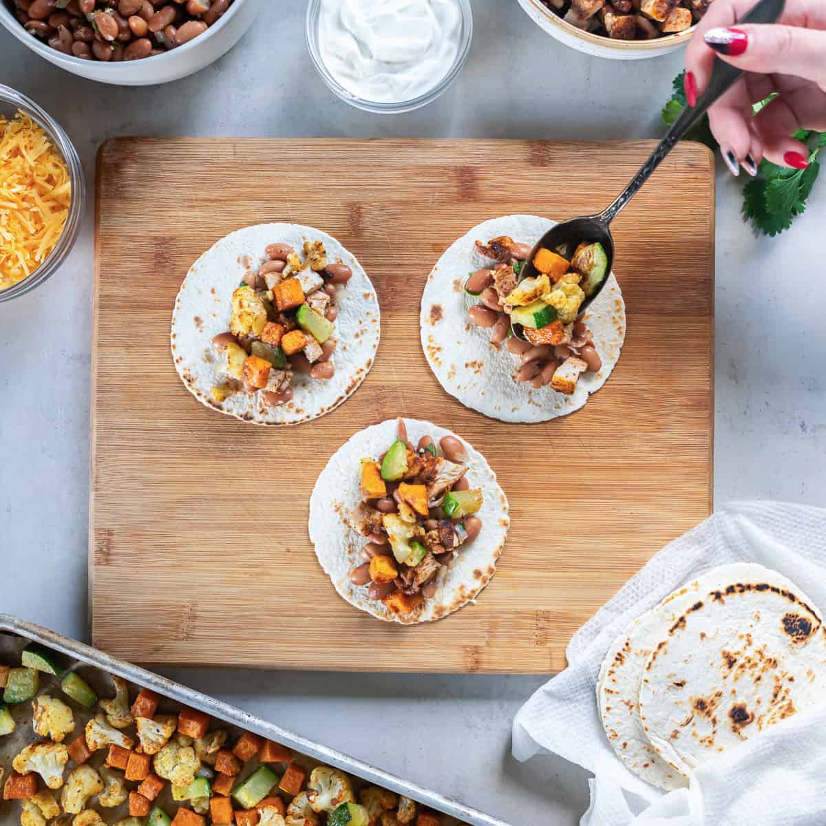 Assembling chicken and roasted veggie tacos with pinto beans, roasted vegetables, and chopped chicken on toasted tortillas.