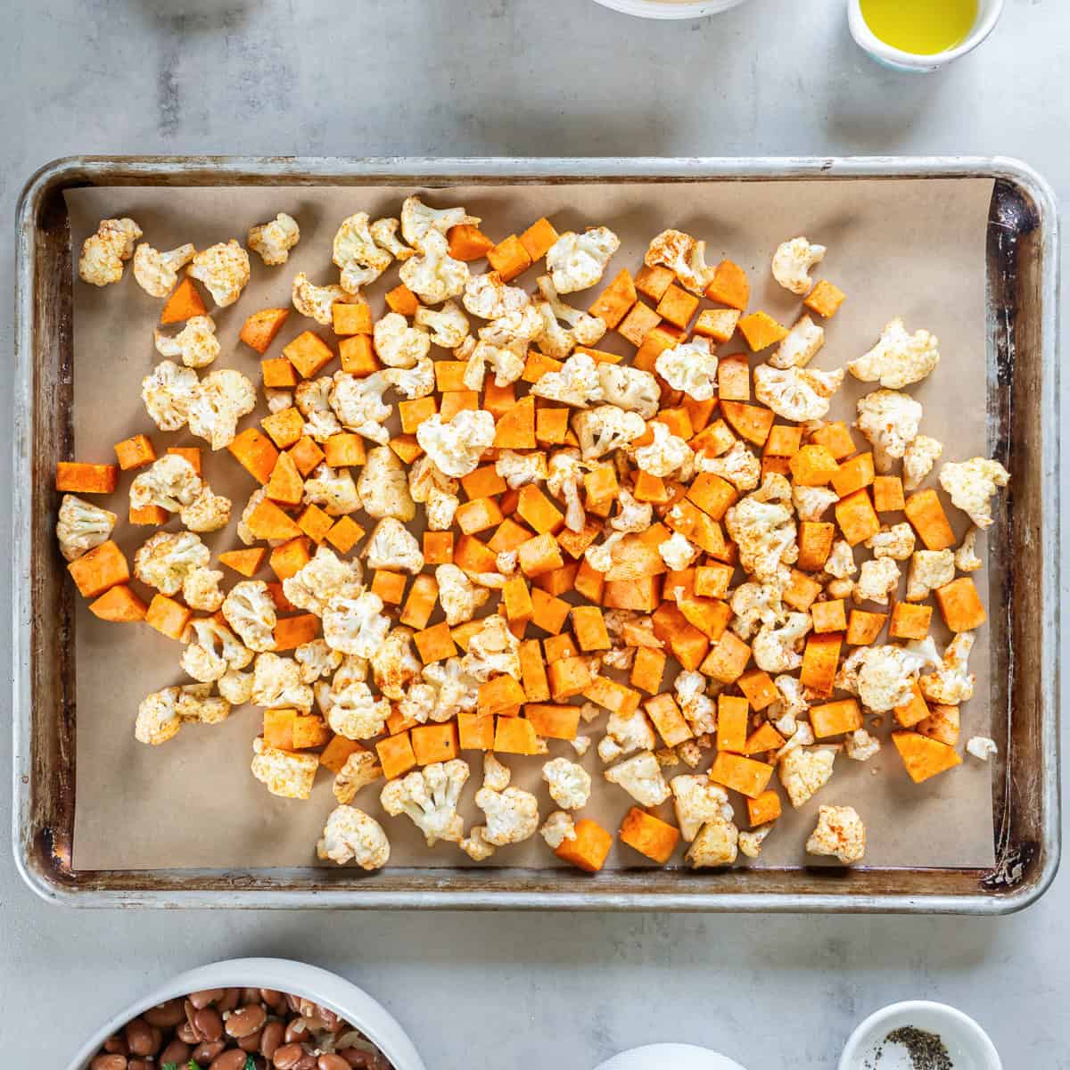 Seasoned sweet potato and cauliflower spread on a parchment-lined baking sheet before roasting.