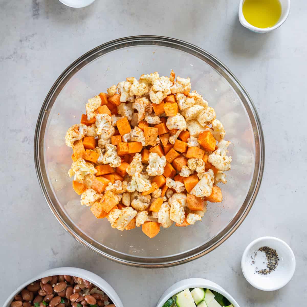 Sweet potato and cauliflower tossed with oil and seasonings in a glass bowl before roasting for chicken and roasted veggie tacos.
