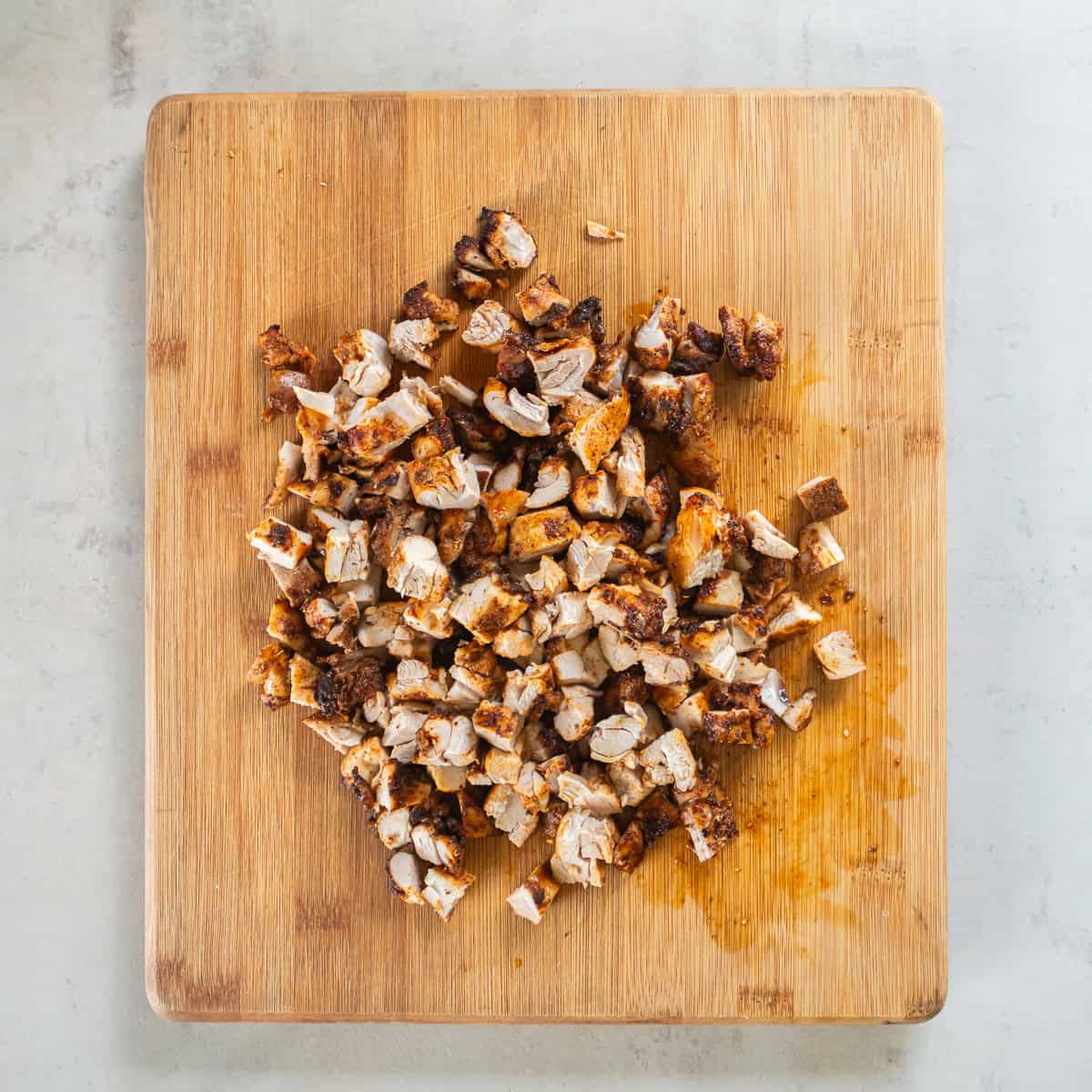 Chopped cooked chicken on a wooden cutting board for chicken and roasted veggie tacos.