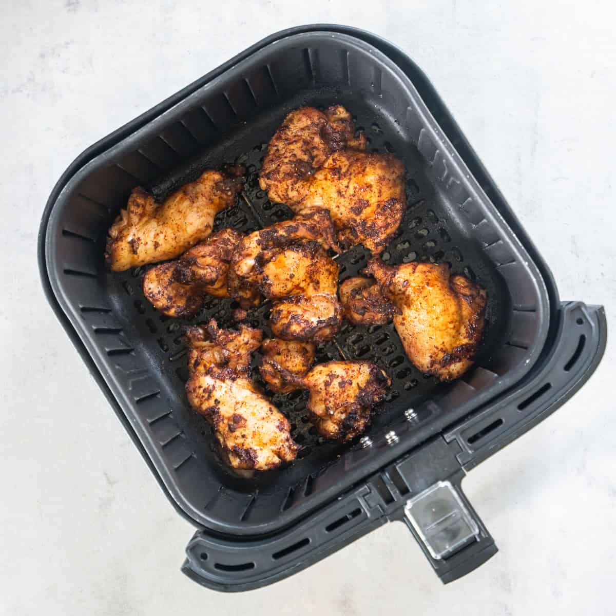 Cooked Mexican-seasoned chicken thighs in an air fryer basket before chopping for tacos.