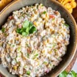 Creamy cold corn dip topped with cilantro and served with Fritos Scoops on a wooden board.