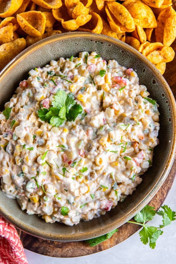 Creamy cold corn dip topped with cilantro and served with Fritos Scoops on a wooden board.