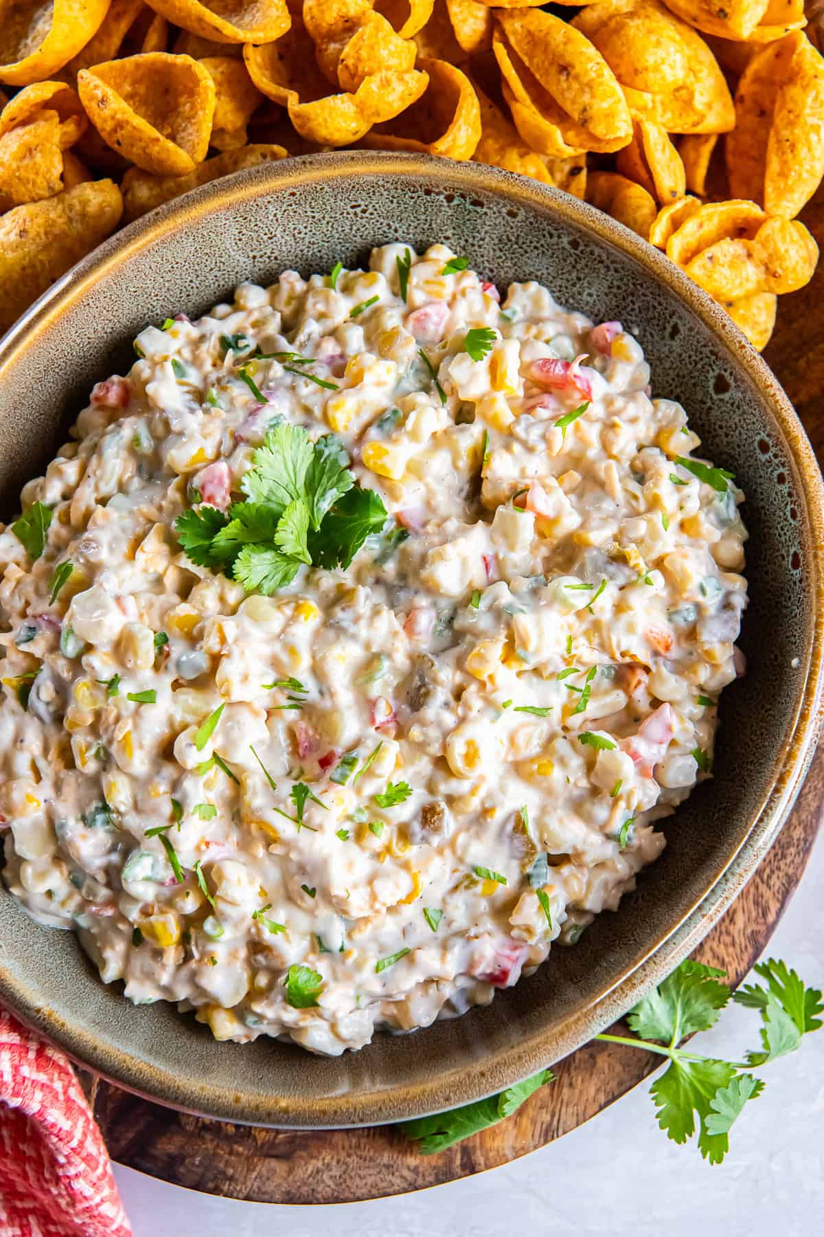 Creamy cold corn dip topped with cilantro and served with Fritos Scoops on a wooden board.
