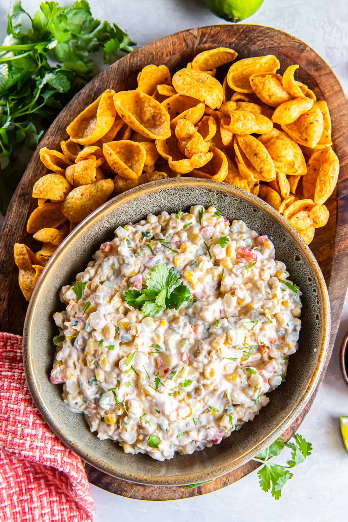 Creamy cold corn dip topped with cilantro and served with Fritos Scoops on a wooden board.