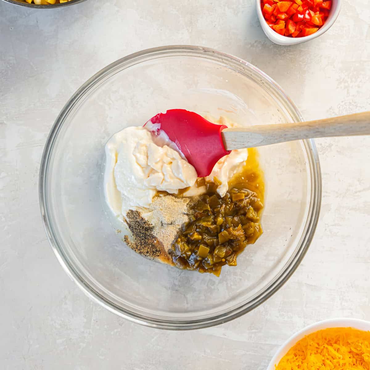 Sour cream, mayonnaise, diced green chiles, lime juice, and seasonings in a mixing bowl for creamy corn dip.