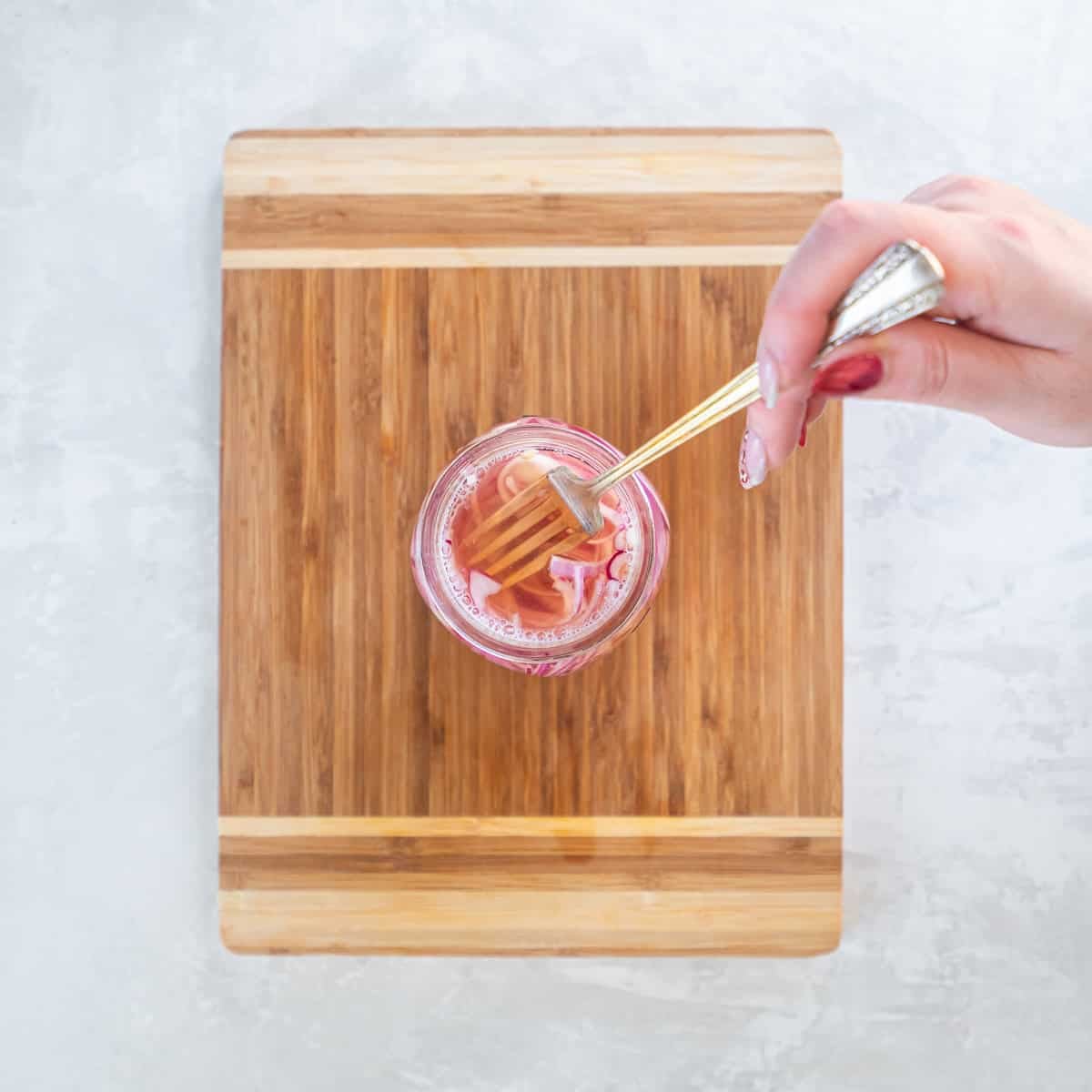 Hand pressing sliced red onions down into pickling brine with a fork in a mason jar.