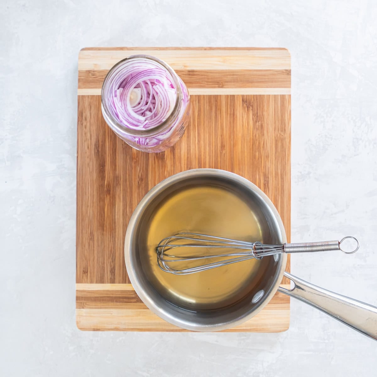 Small saucepan filled with pickling liquid beside a mason jar of sliced red onions.
