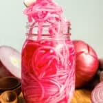Fork lifting quick pickled red onions from a mason jar with fresh red onions in the background.