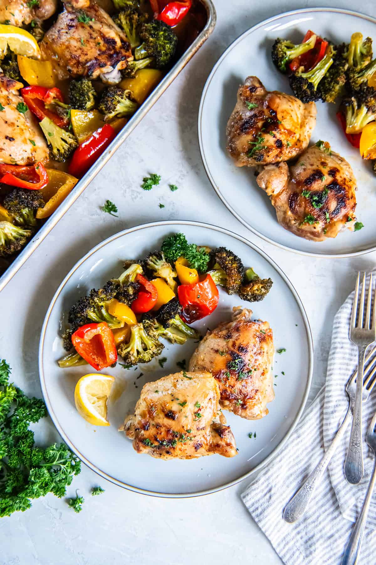 Sheet pan honey mustard chicken served on plates with roasted broccoli and bell peppers, with the sheet pan dinner in the background.