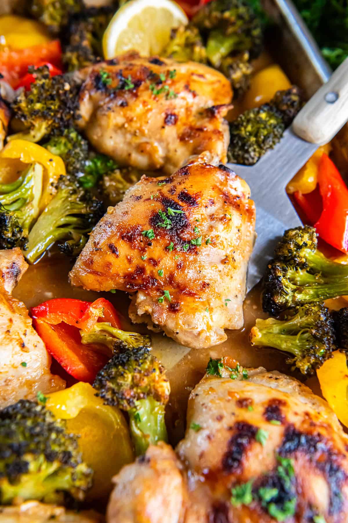 Spatula lifting a Sheet Pan Honey Mustard Chicken Thigh with roasted broccoli and bell peppers from a sheet pan.