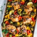 Sheet Pan Honey Mustard Chicken Thighs with roasted broccoli and bell peppers on a sheet pan, garnished with fresh parsley and lemon wedges.