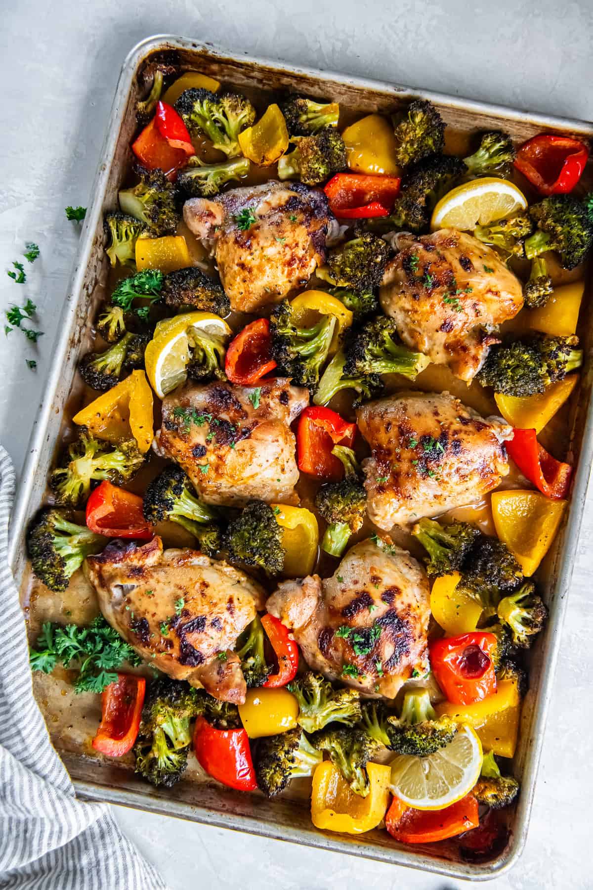 Sheet Pan Honey Mustard Chicken Thighs with roasted broccoli and bell peppers on a sheet pan, garnished with fresh parsley and lemon wedges.