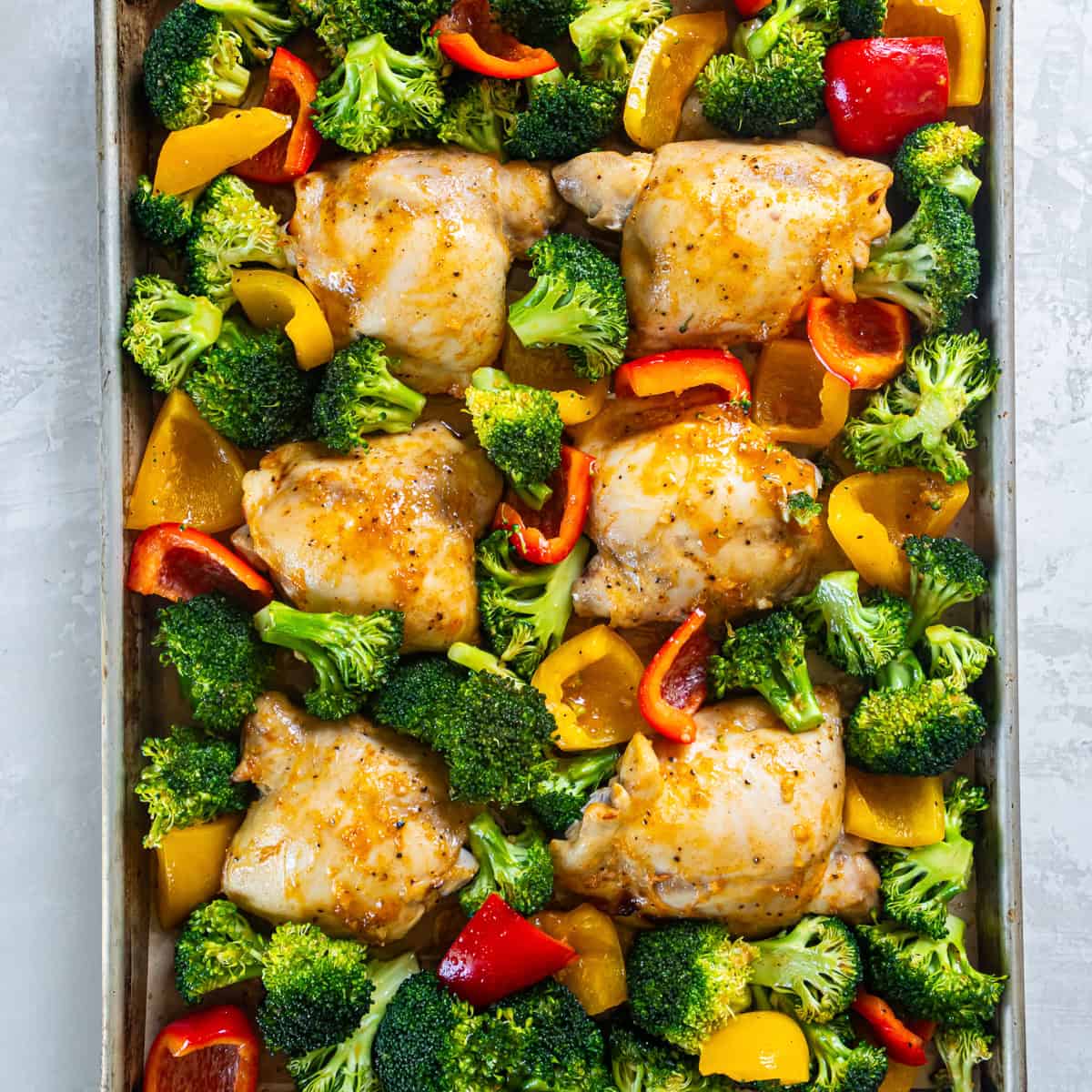 Sheet Pan Honey Mustard Chicken with broccoli and bell peppers arranged on a baking sheet before roasting.