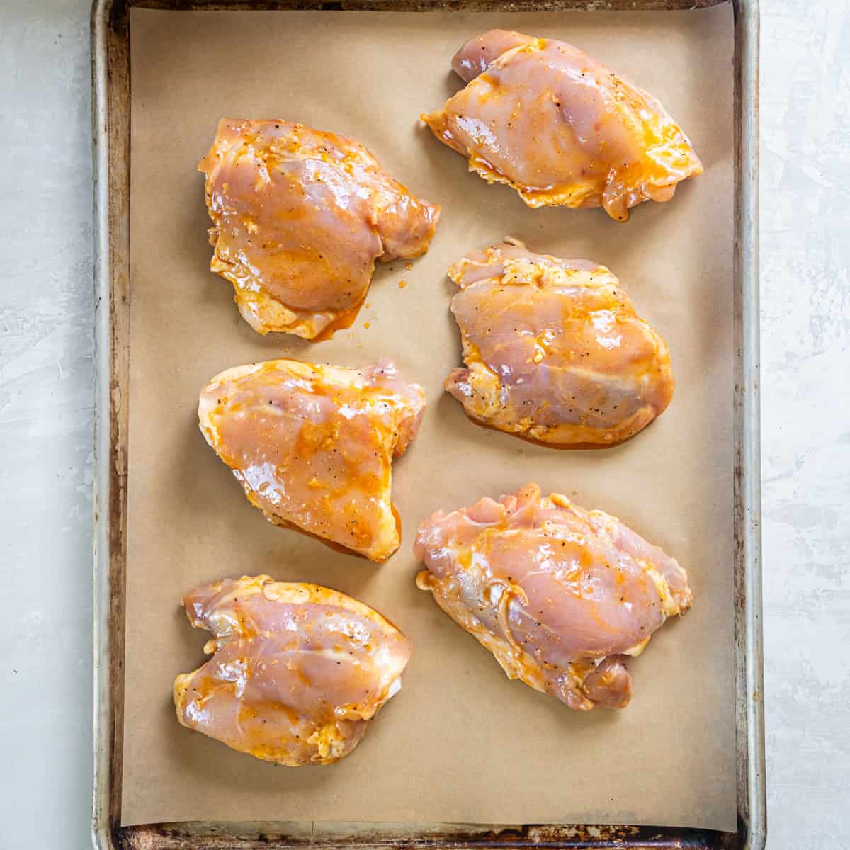 Honey mustard chicken thighs arranged on a parchment-lined baking sheet before roasting.