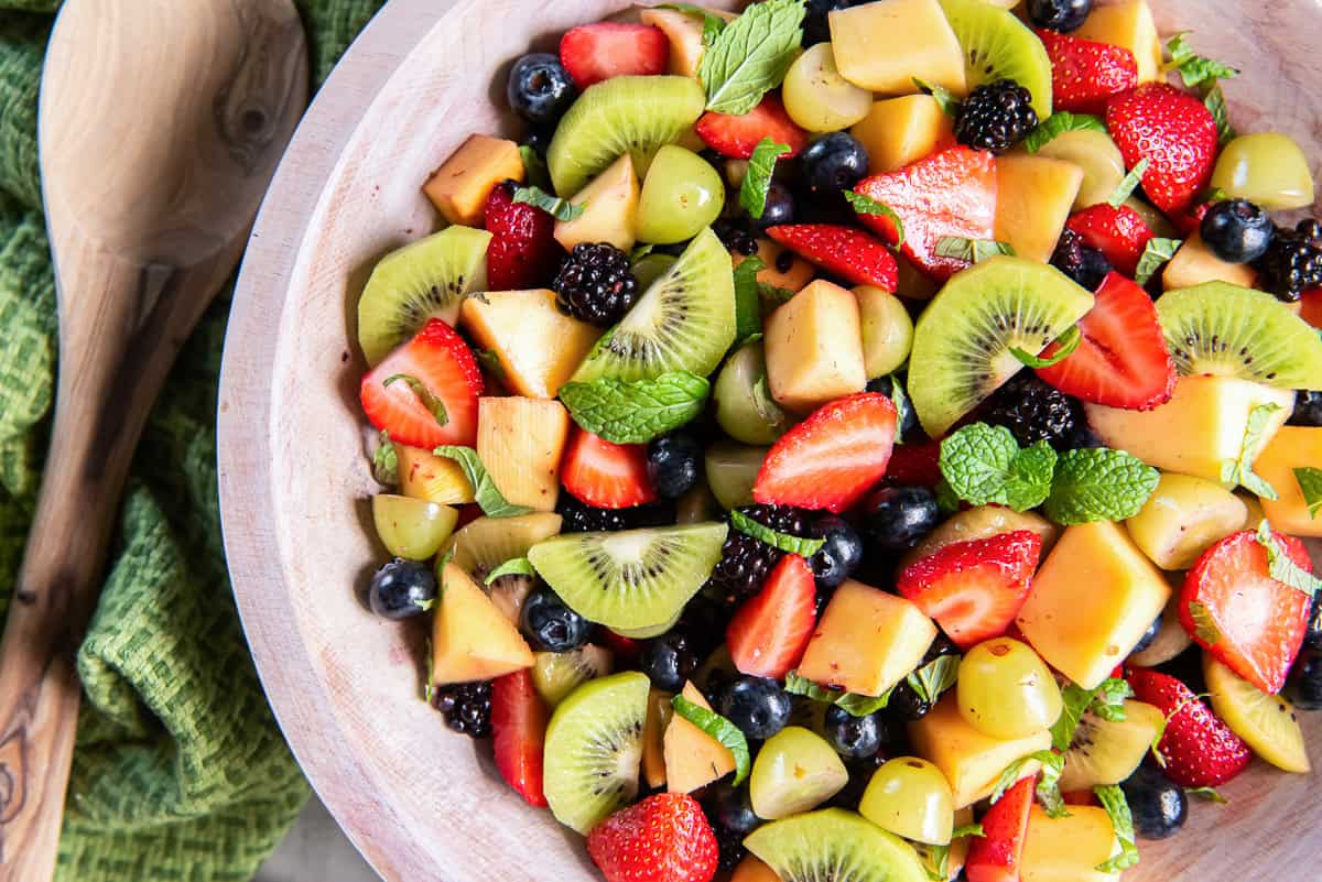 Simple fruit salad with strawberries, kiwi, grapes, mango, blueberries, blackberries, and fresh mint in a wooden serving bowl.