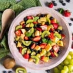 Simple fruit salad with strawberries, blueberries, blackberries, grapes, mango, kiwi, and fresh mint in a wooden bowl.