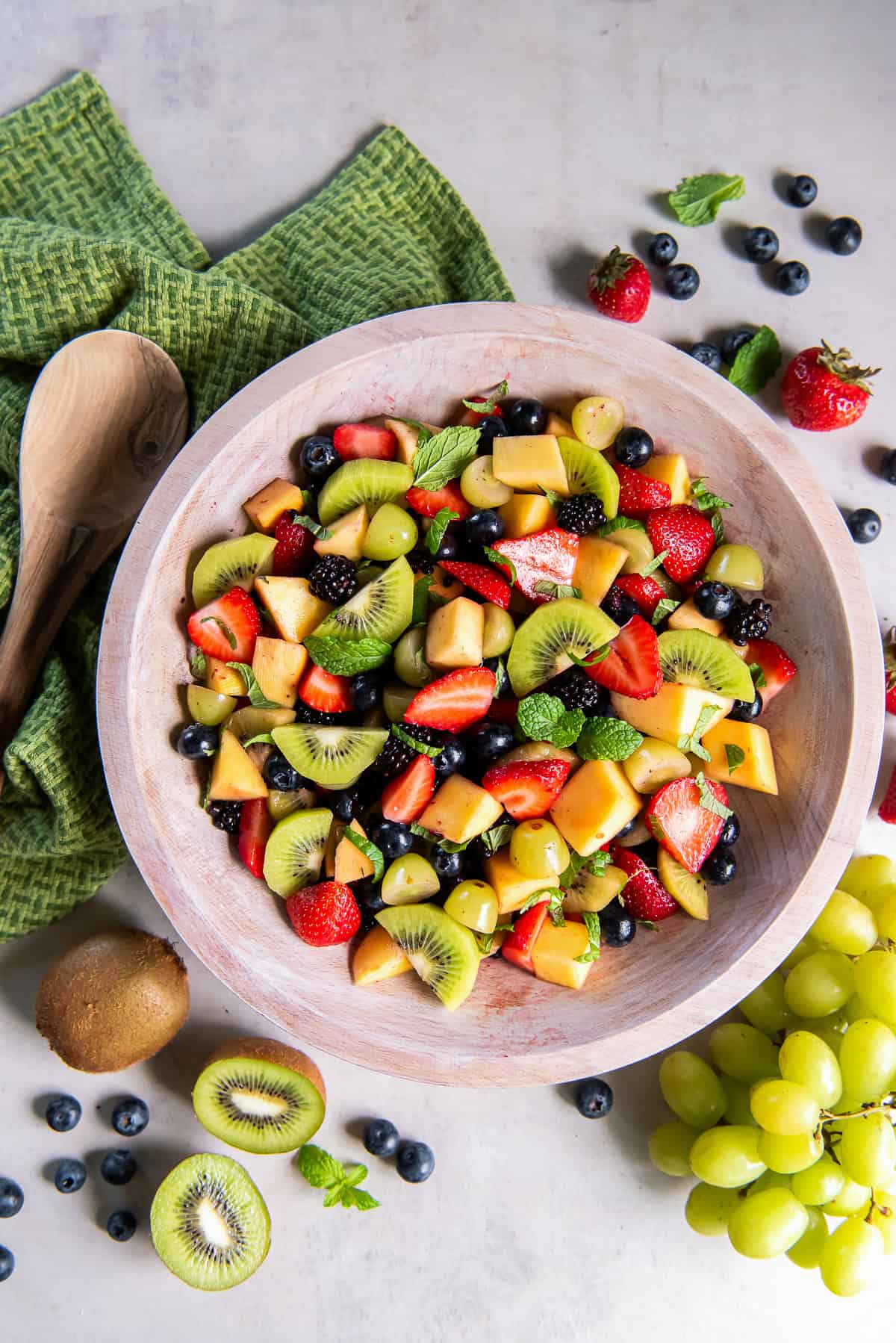 Simple fruit salad with strawberries, blueberries, blackberries, grapes, mango, kiwi, and fresh mint in a wooden bowl.