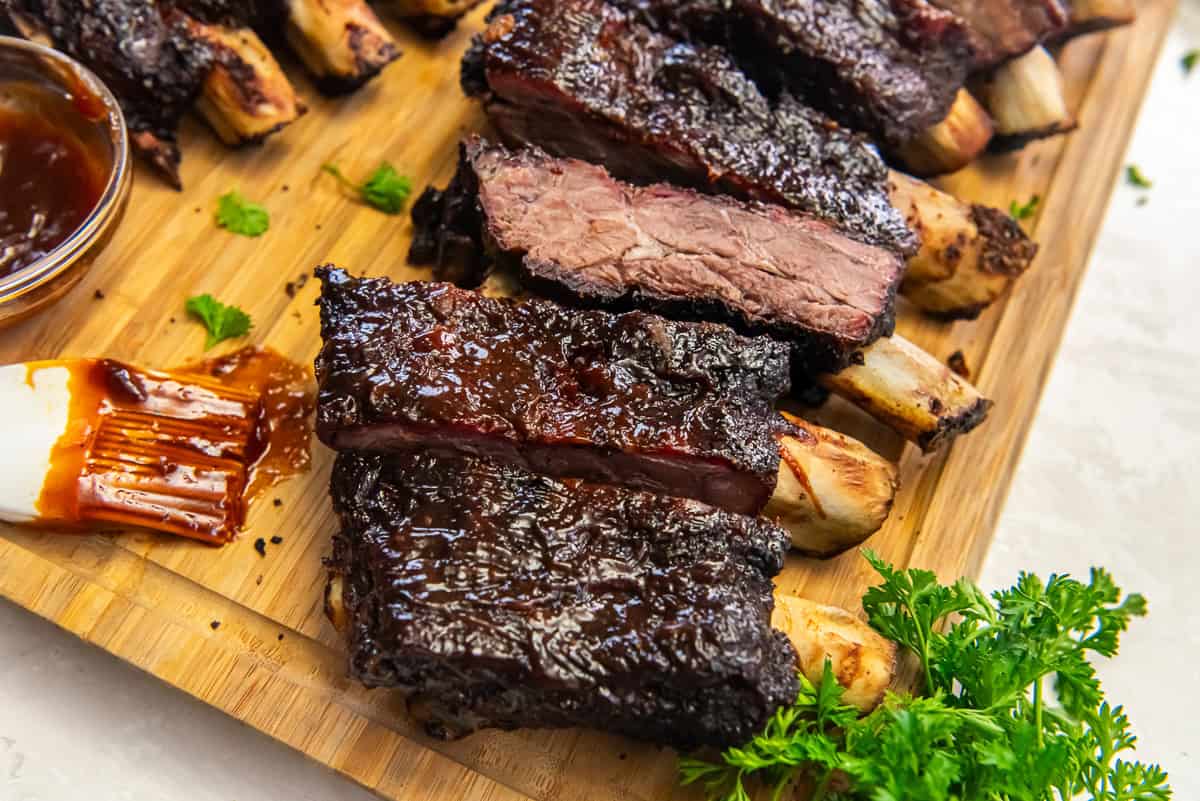 Sliced smoked beef ribs with barbecue sauce arranged on a wooden cutting board.